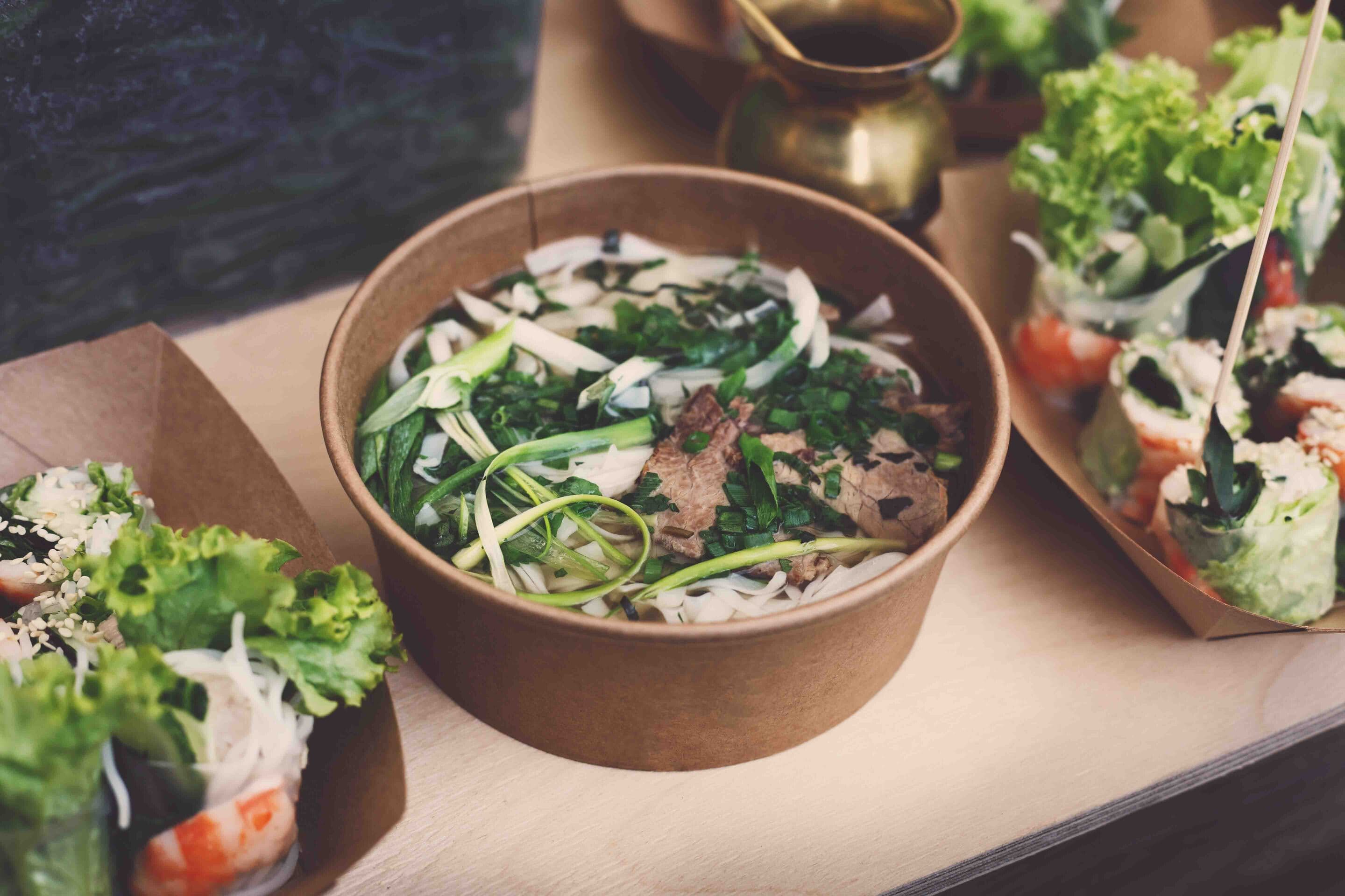 Thai take away street food, tom yam kung soup. Traditional hot spicy curry soup with meat, greenery and noodles, outdoor fast food market