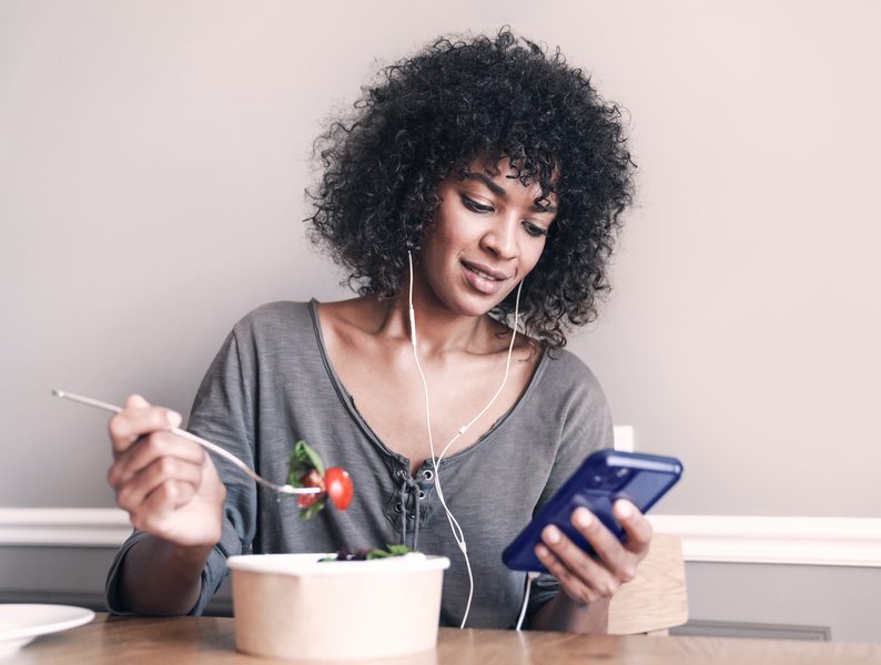 Image of woman using cellphone and earphones while having lunch