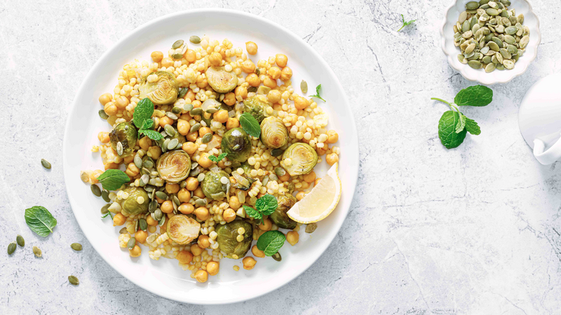 Couscous brussels sprouts and chickpeas warm salad with pumpkin seeds. Healthy vegetarian diet food. Top view